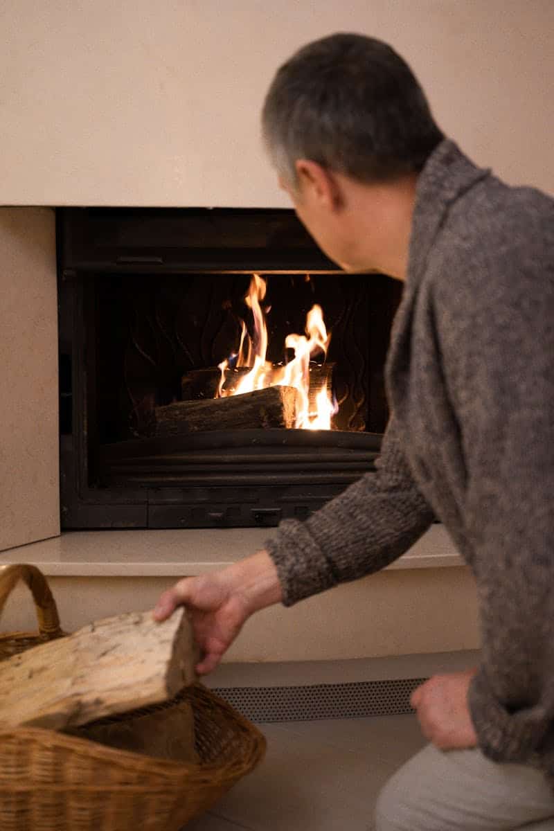 Man adding firewood to a warm, inviting fireplace, creating a cozy home atmosphere.